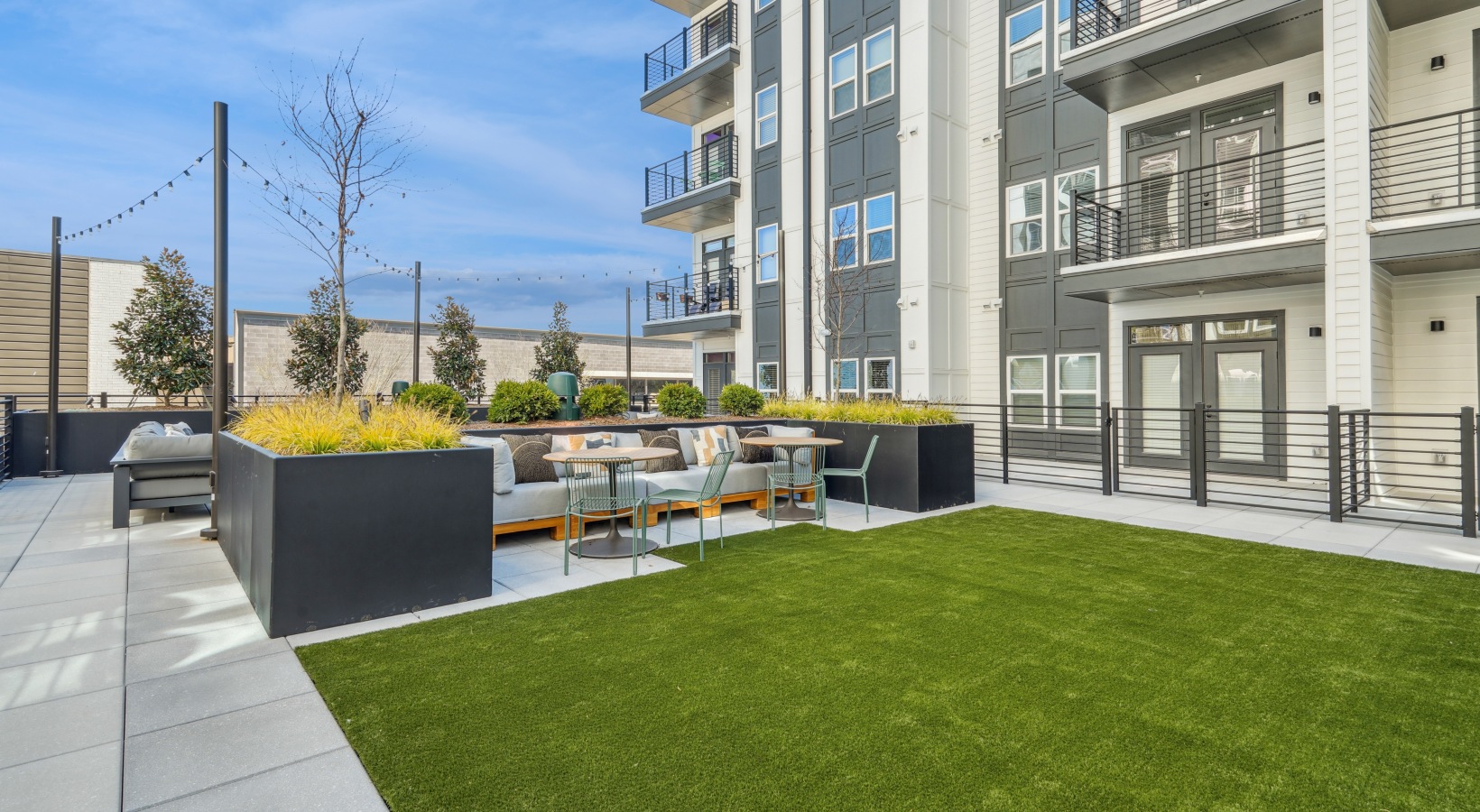 A modern outdoor seating area with grey couches and a fire pit.